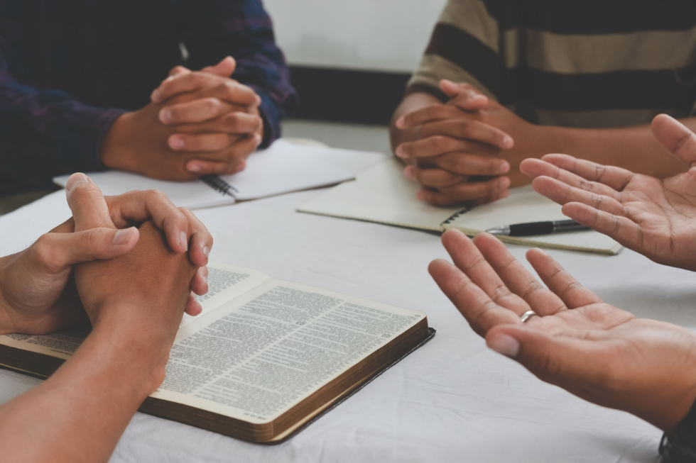 Church leadership team praying around an open Bible while rethinking their fully devoted follower mission statement